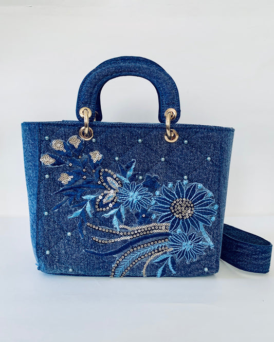 Blue handbag with floral embroidery and embellishments on a white background