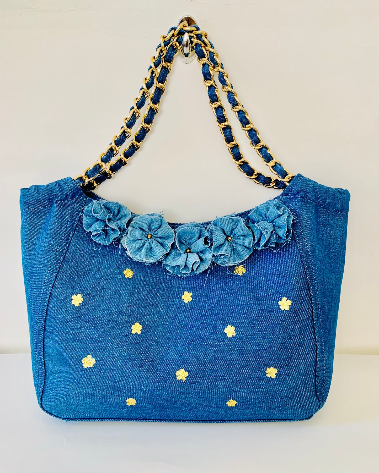 Blue handbag with floral details and gold chain handle on a white background