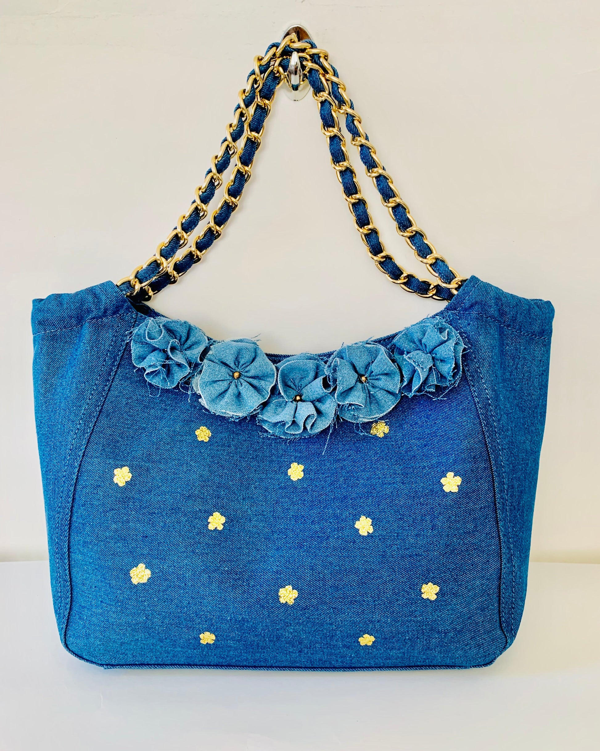 Blue handbag with floral details and gold chain handle on a white background