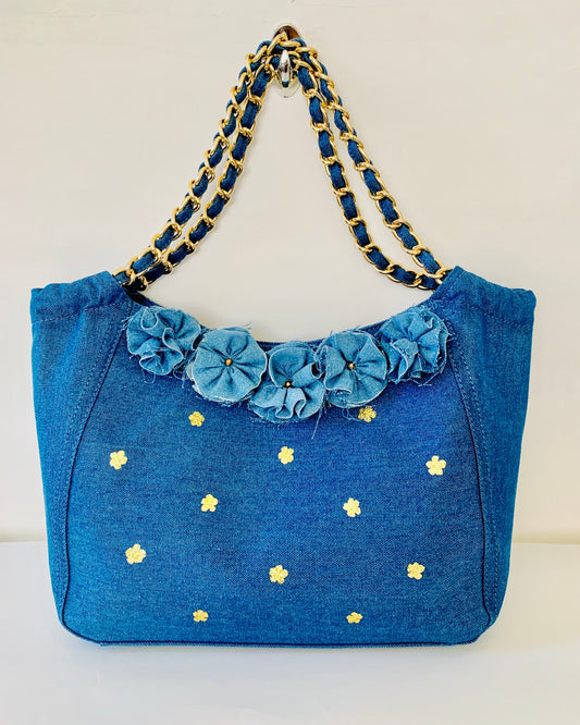 Blue handbag with floral details and gold chain handle on a white background