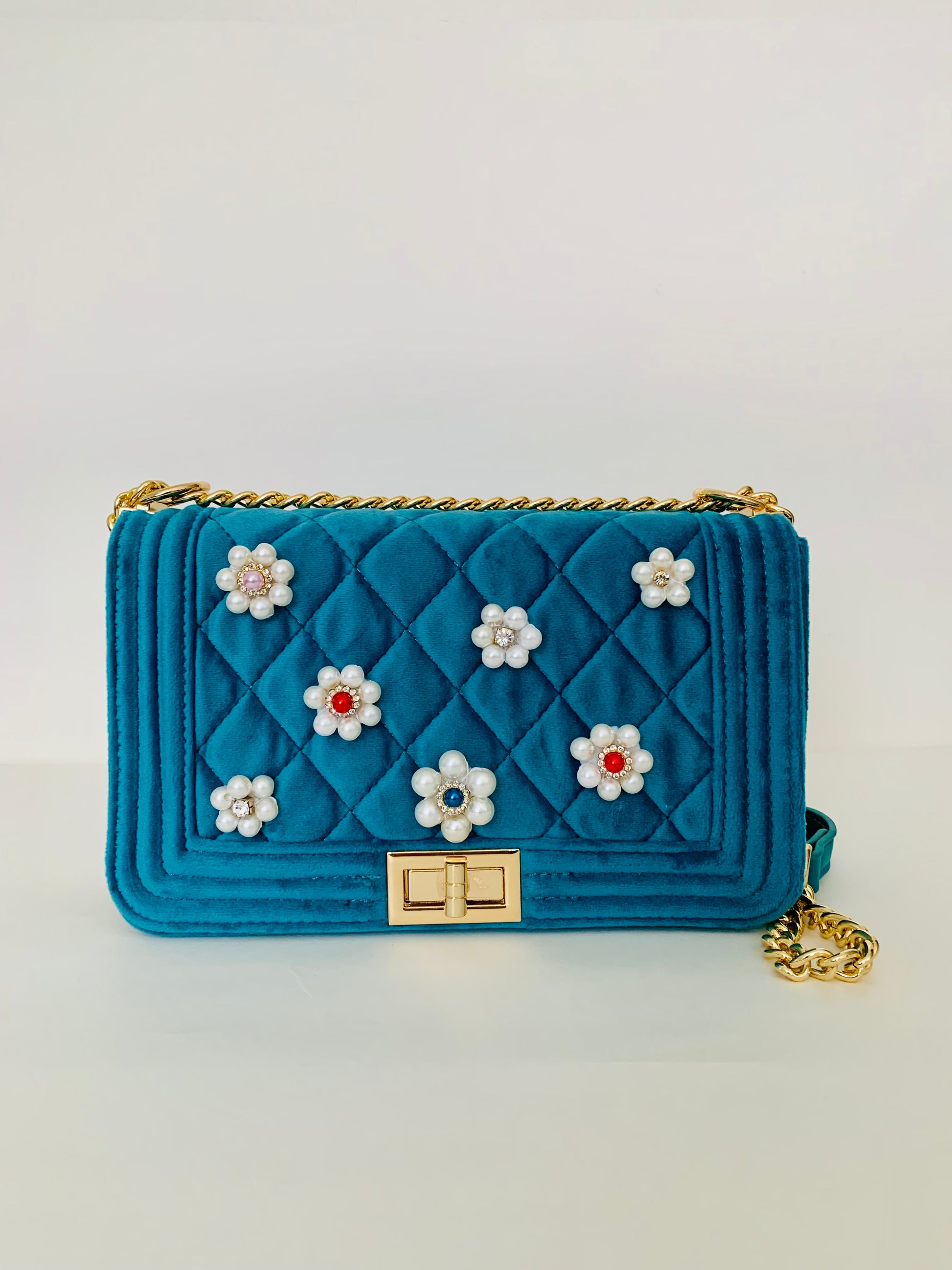 Blue quilted handbag with floral embellishments on a light gray background