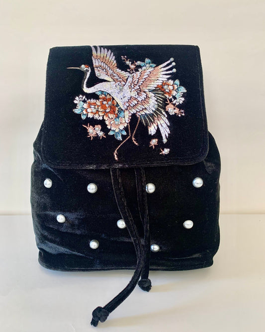 Black velvet backpack with embroidered crane design on a white background